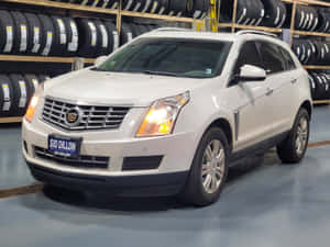 白色Cadillac SRX SUV在室內停放，背景有輪胎架。 — 凱迪拉克 壁紙