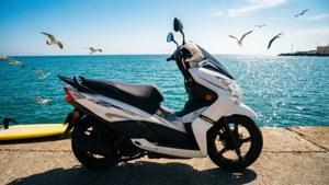 白色機車停在碼頭上，海鷗在海面上飛翔
