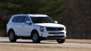 白色Kia Telluride SUV在道路上行駛，樹木呈現動態模糊效果。 — 起亞 壁紙