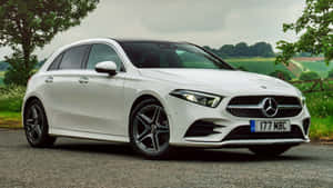 白色 Mercedes-Benz A-Class 停泊在碎石上，靠近綠色田野和樹木。 — Mercedes-Benz 壁紙