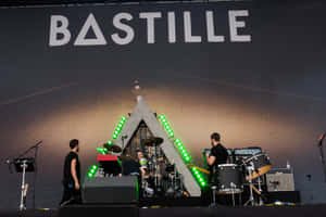 Bastille 樂團在舞台上現場表演，有綠色燈光和三角形背景。 — 巴士底監獄 壁紙