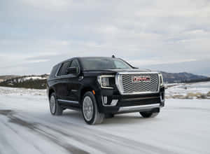 黑色GMC Denali SUV在雪路上快速行駛，背景有山脈。 — 低飽和 壁紙