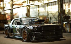 工業車庫內的黑色Hoonigan Mustang甩尾車，金色輪圈。 — MacBook Air M1 壁紙