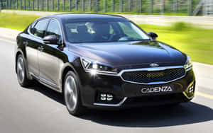 黑色Kia Cadenza轎車在陽光明媚的高速公路上疾馳，背景模糊的綠色植物。 — 馬自達 壁紙