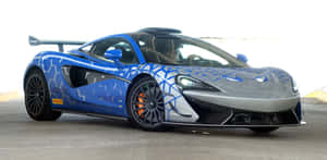一輛帶有幾何圖案貼紙的藍銀色McLaren跑車停在室內。 — 酷炫F1 壁紙