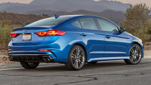 藍色現代 Elantra Sport 停泊在沙漠公路上，日落時分，背後有山脈。 — 可愛的機器人 壁紙