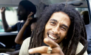 Bob Marley 在車內微笑並指向鏡頭。 — 巴布·馬利語錄 壁紙