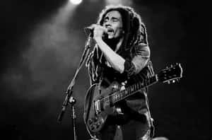 Bob Marley 在舞台燈光下以吉他和麥克風現場表演。 — 巴布·馬利語錄 壁紙