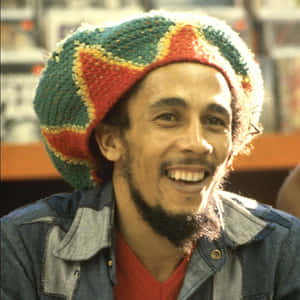 Bob Marley 戴著彩色帽子和牛仔外套，溫暖地微笑。 — 巴布·馬利語錄 壁紙