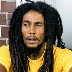 Bob Marley 身穿黃色襯衫靠著磚牆。 — 巴布·馬利語錄 壁紙