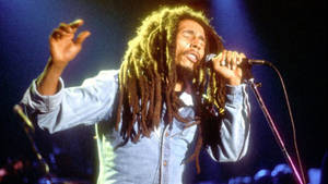 Bob Marley 在舞台上高舉雙臂，閉上眼睛熱情地唱歌。 — 巴布·馬利語錄 壁紙