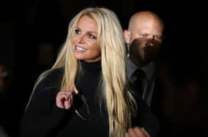 Britney Spears 穿著黑色高領毛衣微笑，身後有穿西裝的男子。 — 小甜甜布蘭妮 壁紙