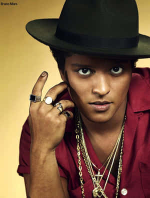 Bruno Mars 戴著黑色軟呢帽和紅色襯衫，佩戴金色珠寶，為照片擺姿勢。 — 3:4 壁紙