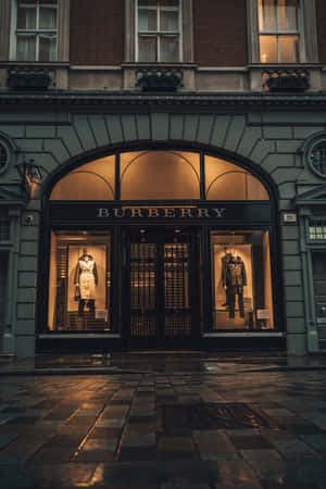 Burberry 店鋪正面，穿著風衣的人體模型在黃昏時在濕漉漉的鵝卵石上發光。 — 榮耀MagicPad 3 壁紙