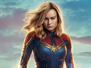 Captain Marvel 穿著她的超級英雄套裝，頭髮被風吹動，背景是多雲的天空。 — 驚奇隊長 壁紙