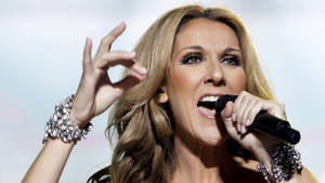Celine Dion 在舞台上唱歌，戴著閃閃發光的手鐲，做出富有表現力的手勢。 — 席琳·狄翁 壁紙