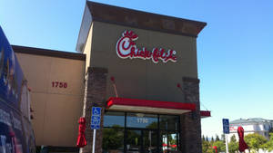 Chick-fil-A 餐廳外觀，在陽光普照的天空下，有紅色遮陽篷和關閉的雨傘。 — 一個 壁紙