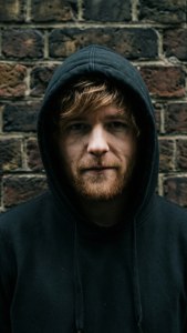 穿黑色連帽衫的男人靠磚牆站立