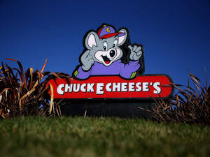 Chuck E Cheese 的吉祥物標誌，卡通老鼠在草地上揮手。