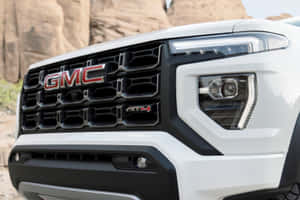 白色GMC AT4卡車前格柵和頭燈在沙漠岩石環境中。 — Surface Pro 壁紙