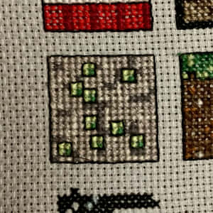 用綠色和紅色線在布料上十字繡的Minecraft方塊。 — iPad 壁紙