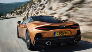 橙色McLaren跑車在山路上高速行駛，背景模糊。 — 福特 壁紙