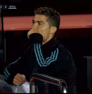 Cristiano Ronaldo 坐在體育場長椅上，身穿帶有青綠色條紋的黑色天鵝絨運動服，手掩著嘴。 — 克里斯蒂亞諾·羅納度 壁紙