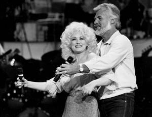 Dolly Parton 和 Kenny Rogers 在音樂會上微笑並在舞台上擁抱。