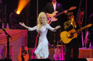 Dolly Parton 在舞台上穿著白色連衣裙唱歌，身後有音樂家。