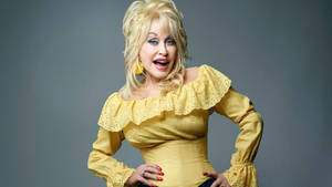 Dolly Parton 身穿黃色荷葉邊襯衫，雙手叉腰擺姿勢。