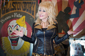 Dolly Parton 身穿金色飾邊的黑色皮夾克，在一個背後有小丑和剪影藝術的音樂節上。 — 桃麗·芭頓 壁紙