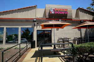 晴朗日子裡，橙色遮陽傘下設有戶外座位的 Dunkin' Donuts 咖啡店。