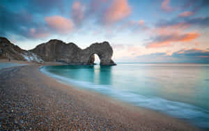 日落時分的 Durdle Door 拱門，平靜的藍綠色海水和鵝卵石海灘。 — 海景 壁紙