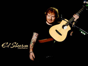 Ed Sheeran 在黑色背景前抱著一把木吉他，紋身清晰可見。 — 紅景天 壁紙