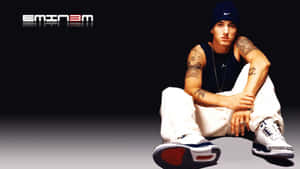 Eminem 盤腿而坐，戴著毛帽和運動鞋，他的名字以文字呈現。 — 阿姆 壁紙