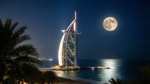 帆船酒店在夜晚滿月下亮起，伴隨著棕櫚樹和海洋。