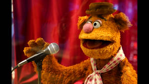 Fozzie Bear 在舞台上表演，手持麥克風，身後有紅色窗簾。 — 可愛熊 壁紙