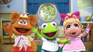 三個 Muppet 角色在色彩繽紛的兒童遊戲室裡揮手。 — 妙妙熊仔 壁紙
