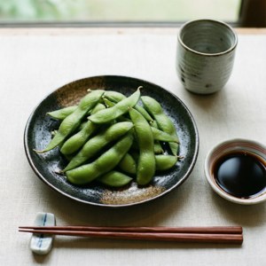 新鮮毛豆配醬油和筷子，置於亞麻桌布上。