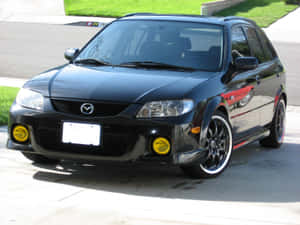 黑色Mazda 3配黃色霧燈，停放在陽光普照的車道上。 — 馬自達 壁紙