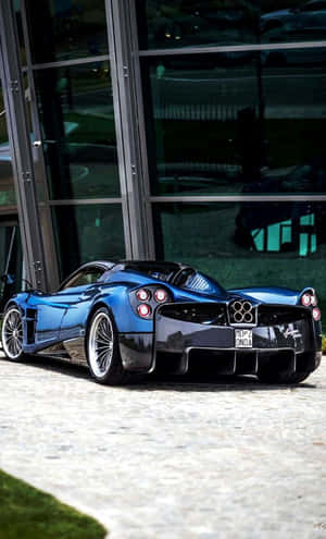 藍色Pagani Huayra停放在玻璃建築旁的石鋪路面上。 — Tecno Megapad 壁紙