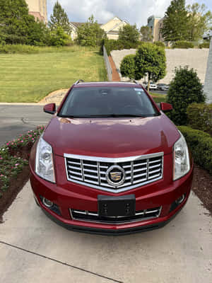 紅色Cadillac SUV停在車道上，後面有綠色草坪和樹木。 — Kindle Paperwhite 壁紙
