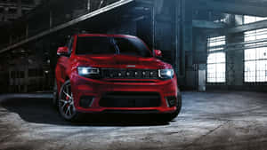 紅色Jeep Wrangler在黑暗的工業倉庫中，車頭燈明亮。 — Studio Display 壁紙