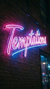 夜晚磚牆上寫著「Temptations」的霓虹燈牌。
