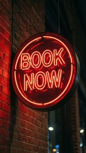 夜晚掛在磚牆上，寫著 book now 的紅色霓虹燈牌。