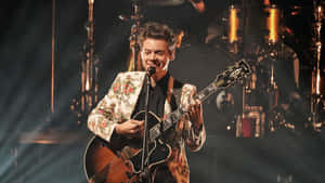 Harry Styles 在現場音樂會表演中於舞台上彈吉他。 — 哈利·史泰爾斯 GIF 壁紙