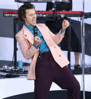 Harry Styles 身穿粉紅色西裝外套和紫色褲子在舞台上表演。 — 榮耀Magic V6 壁紙