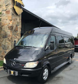 黑色 Mercedes-Benz Sprinter 客貨車停放在石建築物入口處。 — 榮耀Magic V Flip 2 壁紙
