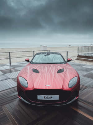 暴風雨天空下，雨中的木製碼頭上的紅色Aston Martin DBS，靠近海灘 — 2048x2732 壁紙