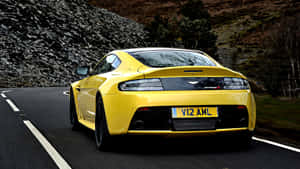 黃色Aston Martin V12 Vantage在日落時分的山路上疾馳。 — 奧斯頓馬丁 壁紙